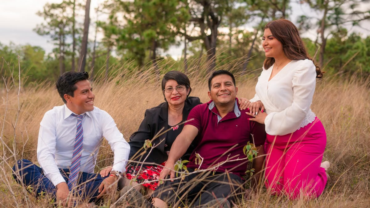 Family portrait of smiling adults sitting in a grassy field, enjoying nature outdoors.